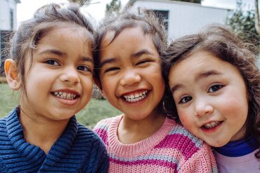 A group of three children smiling broadly