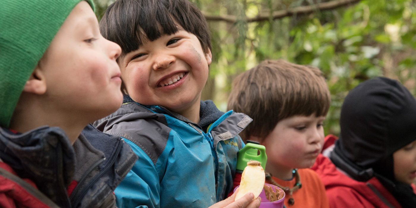 Kids with dirt smudges on their faces, laughing and eating outdoors