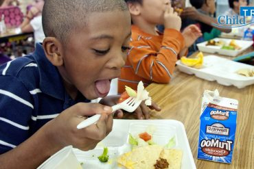 A young boy takes a bite of a school meal