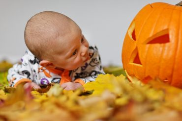 A cute baby looking surprised at a jack o' lantern on some autumn leaves