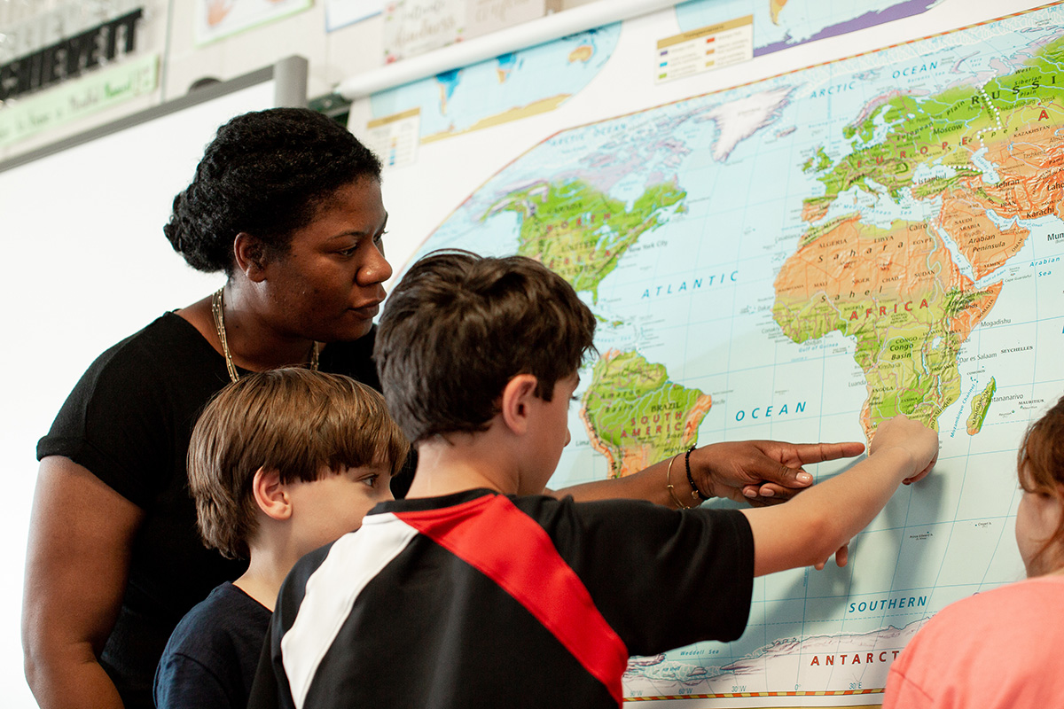A group of children and their teacher/leader point to a global map together