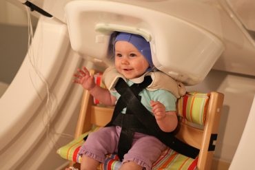 A baby smiles while being tested by a Magnetoencephalography (MEG) machine