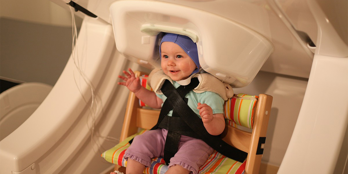 A baby smiles while being tested by a Magnetoencephalography (MEG) machine